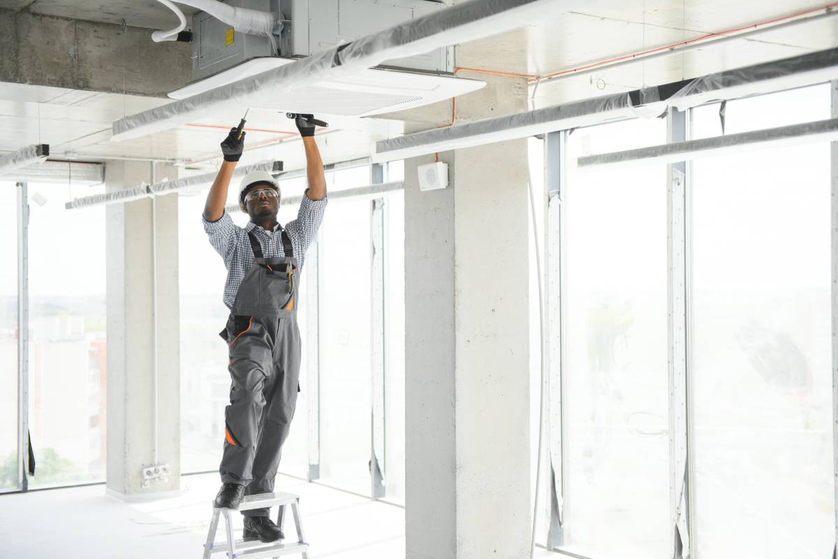 African American electrician repairing air conditioner indoors.