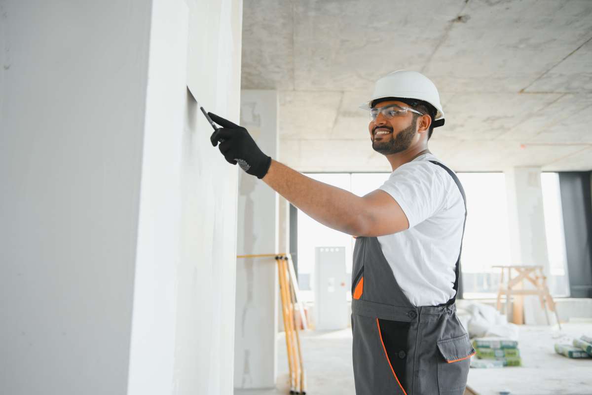 Professional worker plastering wall with putty knife indoors.
