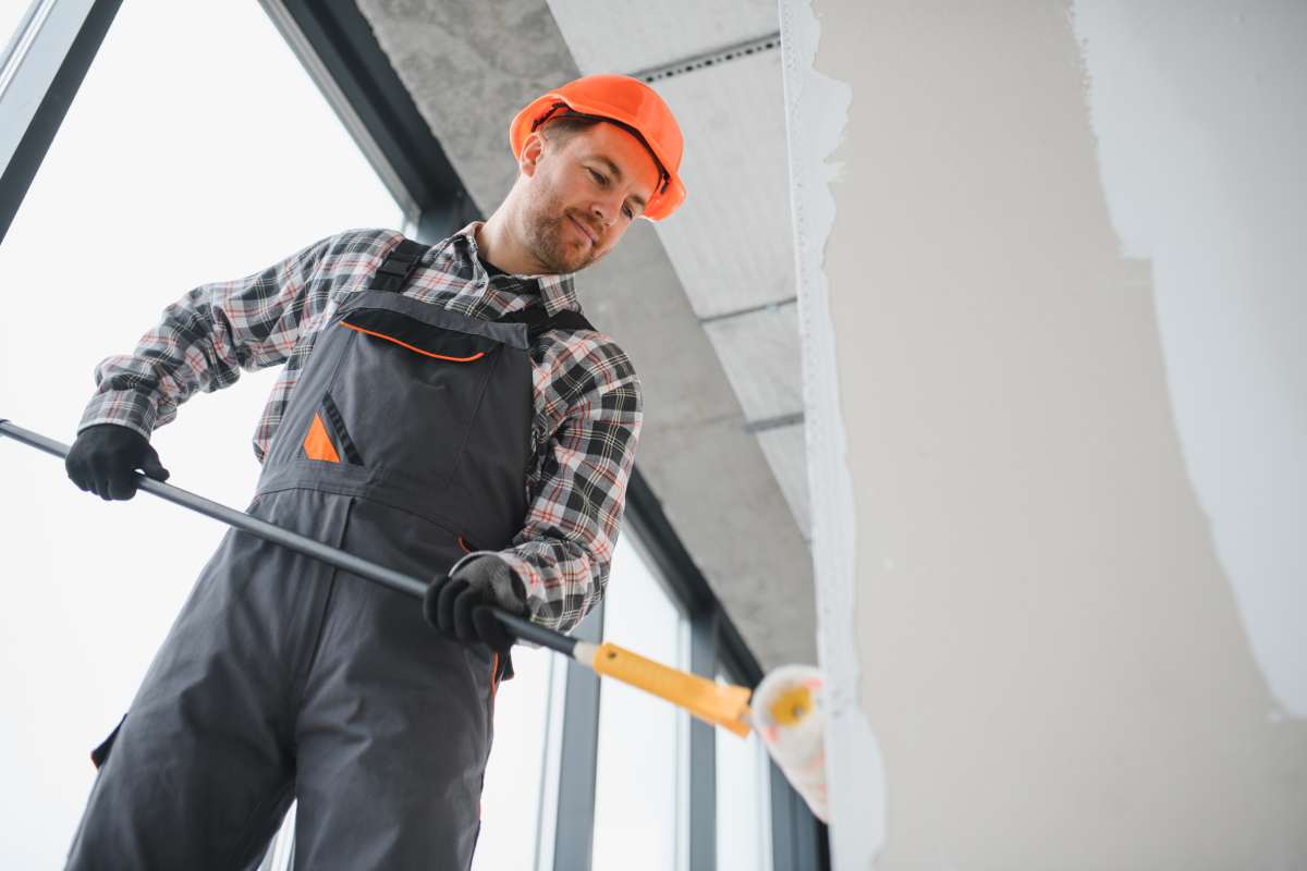 Professional builder using a paint roller, applying a fresh coat of paint to the walls of a building under renovation, demonstrating the process of interior finishing