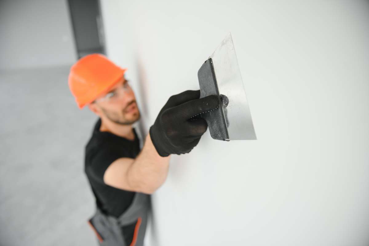 Tradesman on stilts plastering drywall in home.